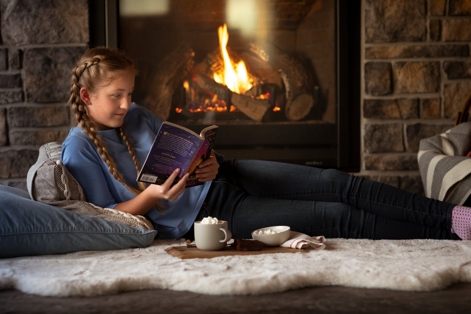 Girl reads a book while laying in front of a fireplace