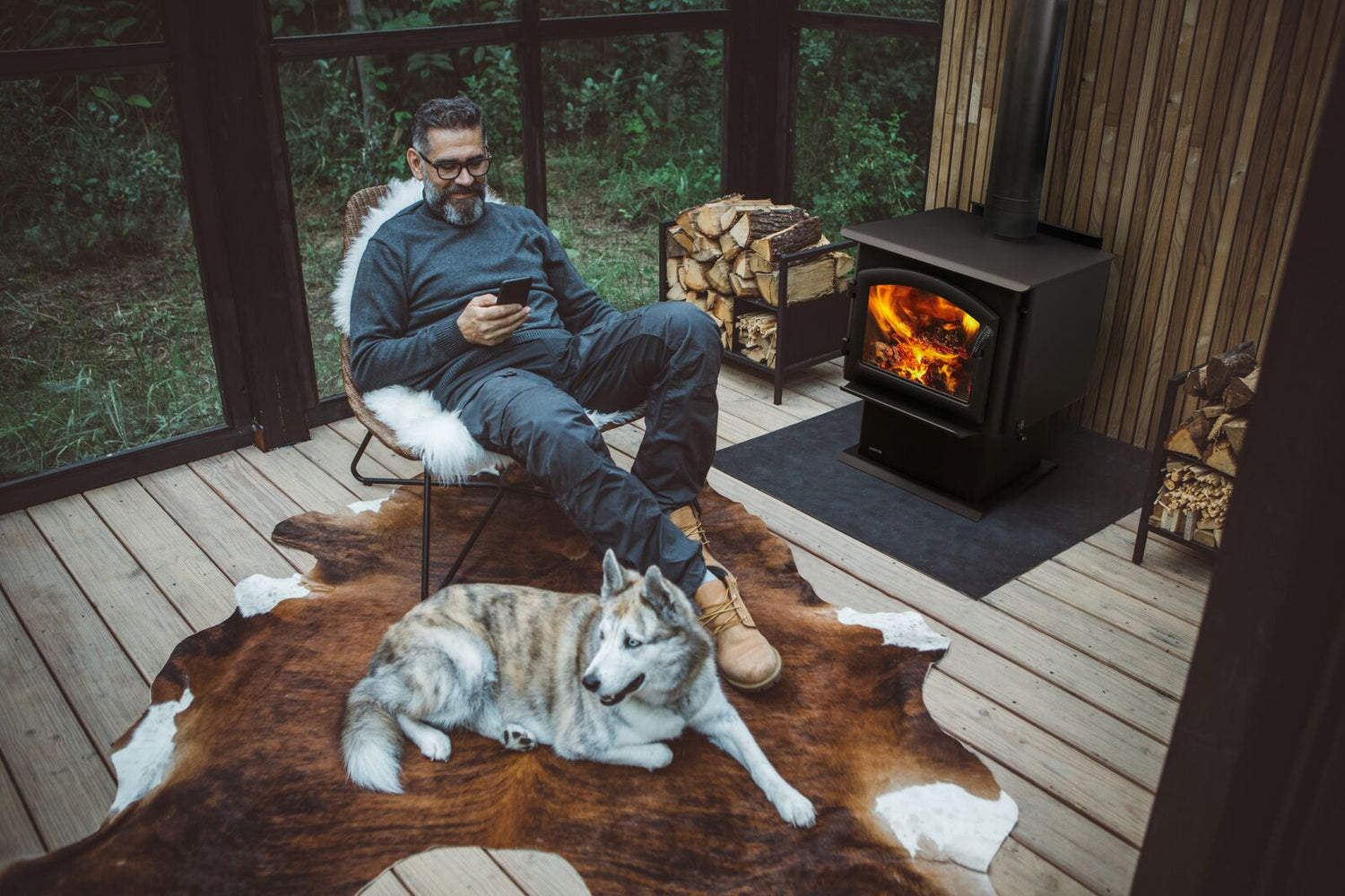 A man sitting near a wood stove with his dog on a porch