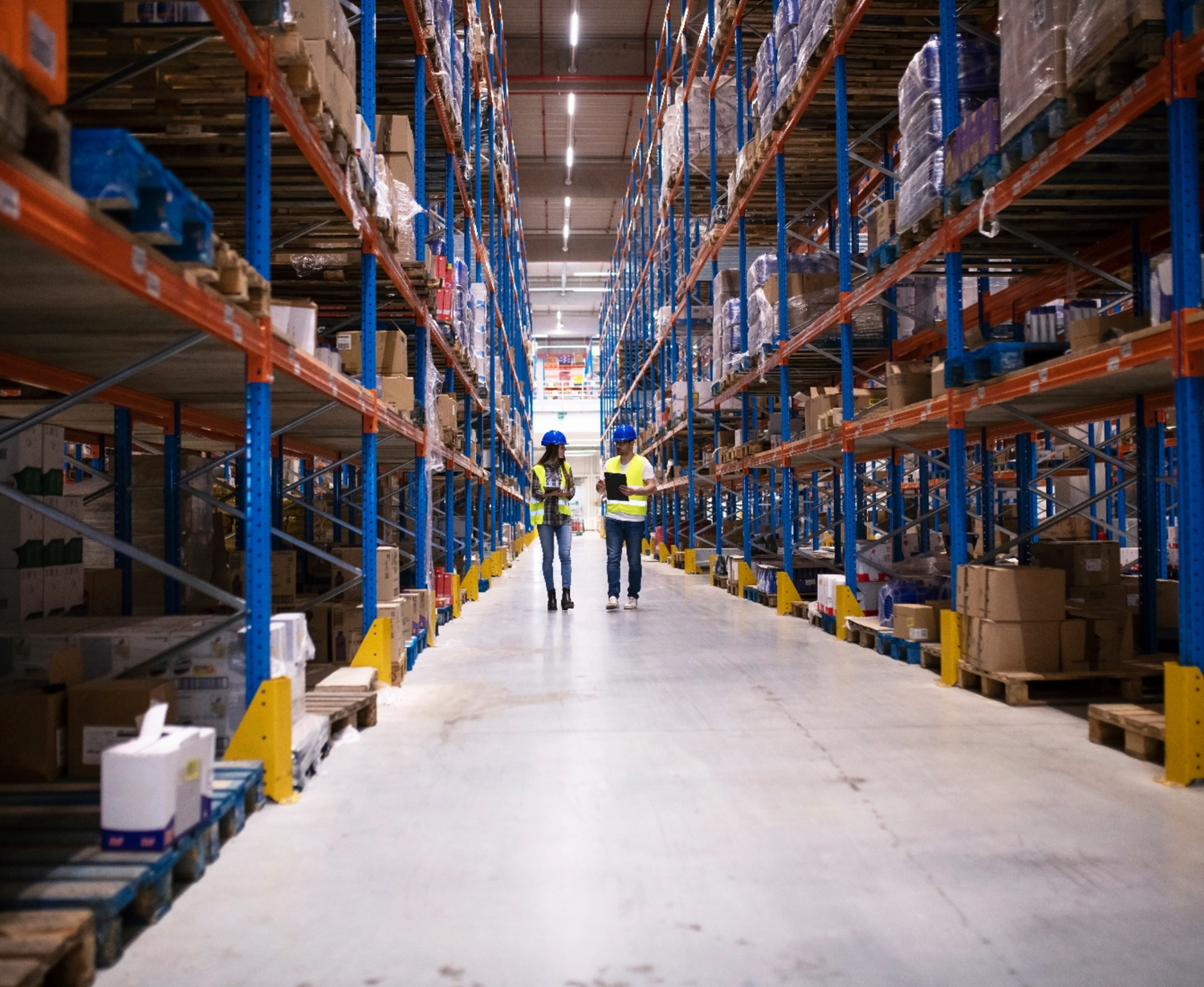 A large warehouse with two employees walking down its aisles